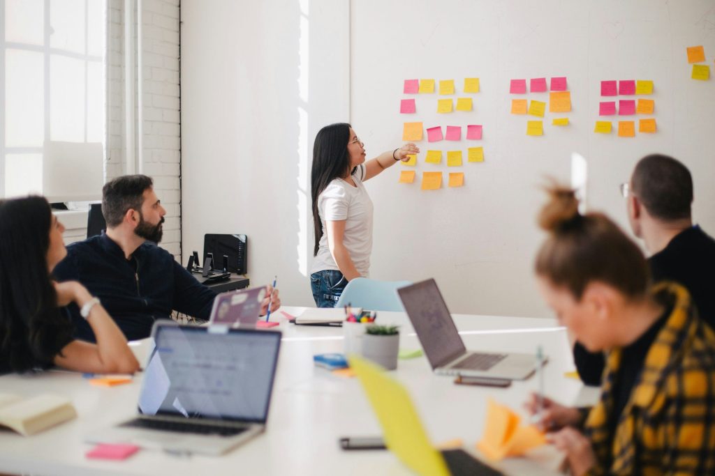 Mujer da una charla en una sala de reuniones señalando post-its en una pared